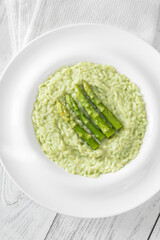 Asparagus risotto served in white plate with whole spears on top