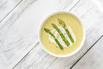 Creamy asparagus soup in white bowl with swirl and toasted ciabatta