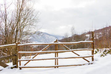 countryside landscape in winter. rustic security. wooden fence through snow covered hill. deciduous forest