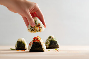 Hand Lifting a Japanese Onigiri. A hand is lifting an onigiri rice ball from a wooden table with more onigiri and some garnish.