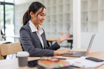 Excited friendly young asian woman 20s in casual clothes sit on desk,  talk work on laptop pc...