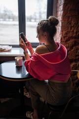 Charming woman with beautiful smile reading good news on mobile phone during rest in coffee shop, happy Caucasian female watching her photo on cell telephone while relaxing in cafe during free time 