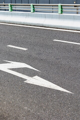 Empty urban asphalt road with white arrow markings and green barriers