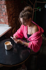 A stylish woman enjoying her coffee while scrolling on her phone in a warm cafe setting.