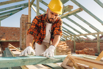 Measuring and marking the plank. Construction worker is on the roof of a house