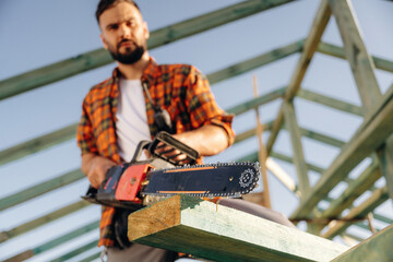 Front view, with chainsaw. Construction worker is on the roof of a house