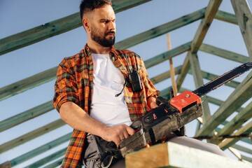 Powerful chainsaw. Construction worker is on the roof of a house