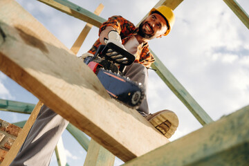 View from below, cutting plank by chainsaw. Construction worker is on the roof of a house