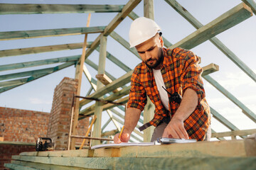 With a plan on paper. Construction worker is on the roof of a house