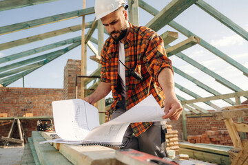 Plan of the building in hands. Construction worker is on the roof of a house