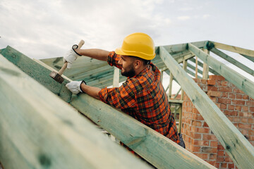 Hammer in hand, standing high up. Construction worker is on the roof of a house
