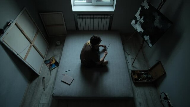 Time passing in creative space. Young artist lies, sits, writes, stares at painting, reflecting procrastination and inner struggle.
