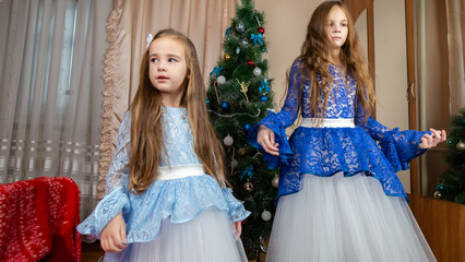 Little girls in festive dress dancing near christmas tree at home