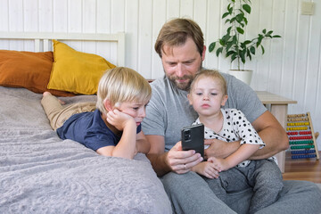 Young dad using smartphone with his kids. Man watching something in a smartphone. Happy father,...