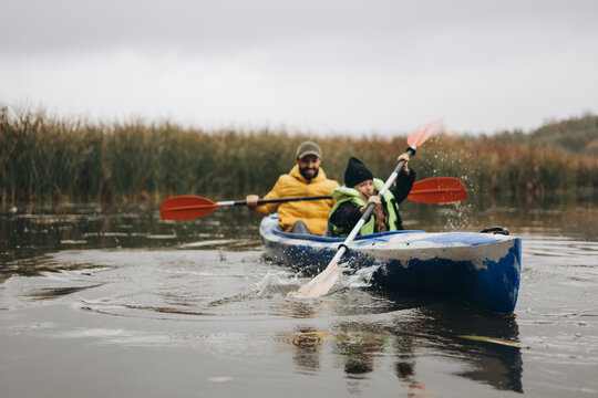 A young father and his little girl canoe together in the middle of a river in an autumn forest. A father and daughter's weekend together
