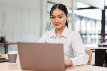 Smiling asian female marketing manager, professional it specialist working, browsing at laptop computer sitting at desk in modern office. Cheerful young woman employee work for business 