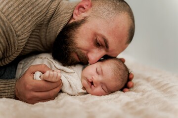A tender moment between a father and his newborn baby, both lying on a soft surface. The father is...