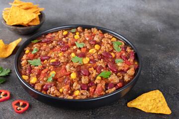 Meat mexican stew with beans, corn and tortilla chips chili con carne on gray background. Tex-Mex...