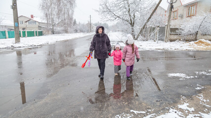 Grandmother and girls walk along a snowy street in winter