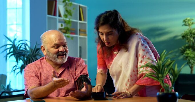Senior couple measuring blood pressure at home using digital BP monitor sitting together at the table, Indian retired family happy with healthy readings, wellness, aging, healthcare lifestyle concept