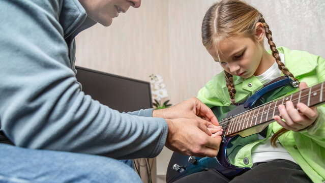 Music teacher and teenage student girl sitting on sofa learning to play on guitar in private lesson in living room at home - Powered by Adobe