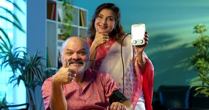 Senior couple measuring blood pressure at home using digital BP monitor sitting together at the table, Indian retired family happy with healthy readings, wellness, aging, healthcare lifestyle concept