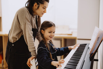 A young girl learning to play the piano with guidance from a teacher.
