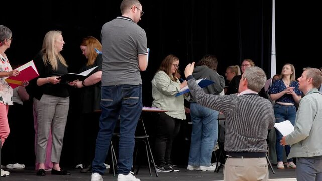 Group of amateur theatre actors rehearsing on stage with scripts, guided by a director. Creative community performance preparation on black stage with props