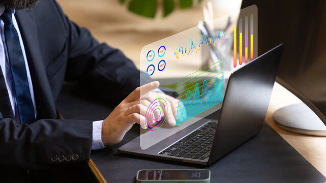 Close-up of suited man's hand operating a digital transparent screen with graphs and analytics on a laptop. Futuristic office setting with advanced technology in business operations.