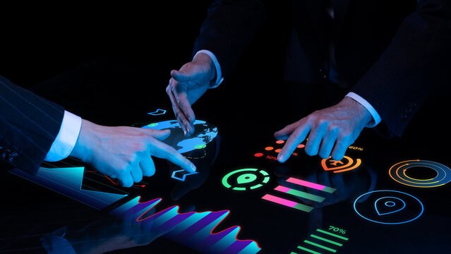 Multiple hands in suits interact with glowing touch table featuring maps, graphs, icons, and digital metrics for business intelligence. Concept of global business, economic trend mapping