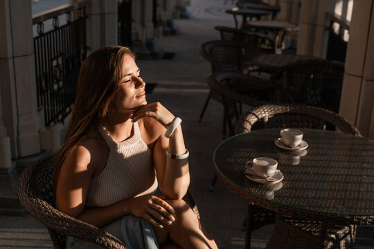 Woman Cafe Table Sunset - A woman sits at a table in a cafe on a sunny day. She appears to be enjoying a cup of coffee and the view. - Powered by Adobe