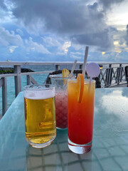Three refreshing drinks, including beer and colorful cocktails, sit on a table overlooking the...