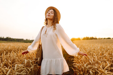 Joyful woman in white dress posing in golden wheat field. Young woman having fun and enjoying sunny...