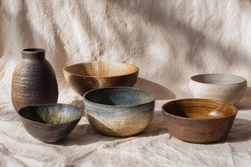 Assortment of artisanal ceramic bowls and vases in neutral glazes on wrinkled linen cloth