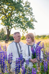 Smiling mature Ukrainian couple wearing vyshyvanka shirts and holding lupine flowers, standing...