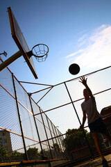 Young guy throws a ball into a basketball hoop on a yard court