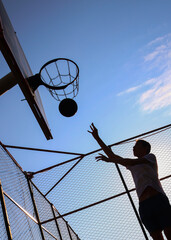 Young guy throws a ball into a basketball hoop on a yard court