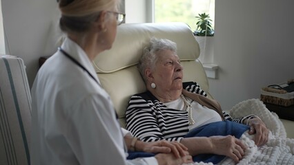 An elderly woman sits comfortably in her home, chatting with a healthcare provider. They share a moment of connection and support in a cozy atmosphere.