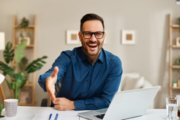 Smiling businessman offering handshake during video conference at home office
