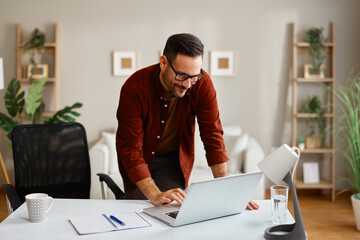 Freelancer working from home office standing at desk typing on laptop