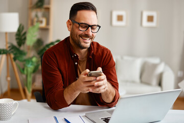 Happy entrepreneur using smartphone and laptop at home office