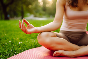 Young woman meditating on mat in sunny park. Sporty woman relaxing, doing exercises on green meadow...