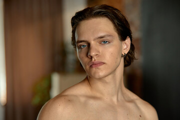 A confident young Caucasian man with short hair poses indoors against a soft blurred background....