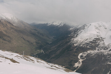 View of the snow-covered peaks of the Caucasus Mountains. The sun is covered by clouds. It is cloudy