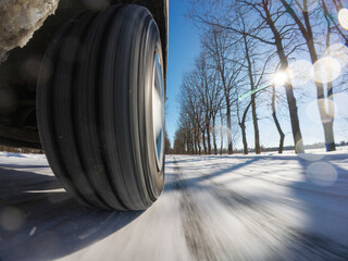Car wheel on a snowy road under the winter sun. A moving car wheel on a winter road, symbolizing...