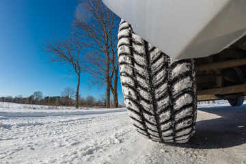 Winter tire tread on snow on a sunny day. Detailed view of a winter tire providing traction on a...