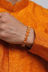 A man's hand with a yellow rakhi on his wrist. Traditional festive attire in golden yellow tones.