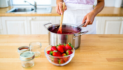 Woman making sweet strawberry jam in kitchen. Person in apron pouring homemade raspberry jam into jars. Strawberry season. Summer recipe. Organic, fresh berry jam