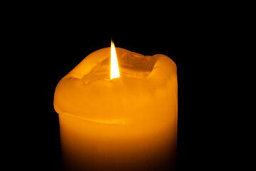 Single burning candle in darkness – glowing flame with melted wax and black background