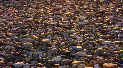 Sunlit pebble beach. Smooth stones are illuminated by warm sunlight. Beautiful interplay of colors and textures. Theme related to zen and relaxation.